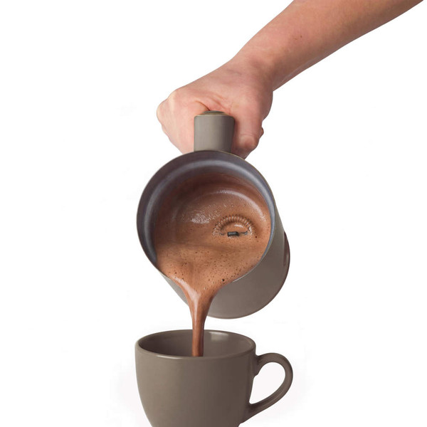 Pouring hot chocolate from a frother into brown ceramic mug