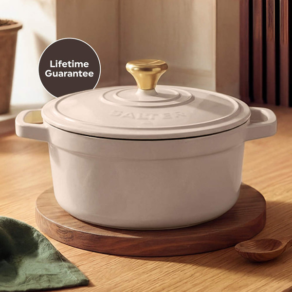 Cream cast iron casserole dish serving vegetable stew, with bowls and bread roll.