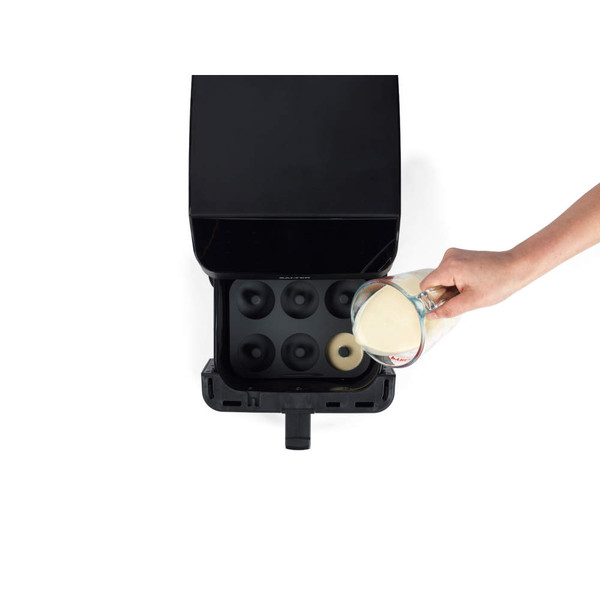 Hand pouring batter into electric donut maker with six moulds, viewed from above