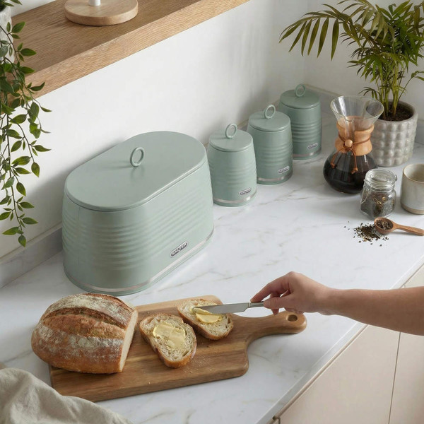 Green bread bin and canisters on kitchen counter, hand buttering sliced bread.