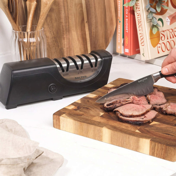 Electric knife sharpener in black on kitchen counter beside hand slicing roast beef
