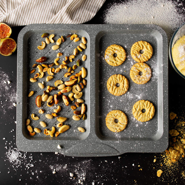 Grey non-stick baking tray with two sections, filled with mixed nuts and round biscuits.