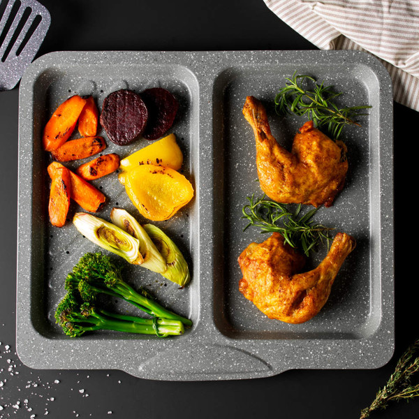 Grey non-stick oven tray with roast chicken legs, mixed vegetables and herbs