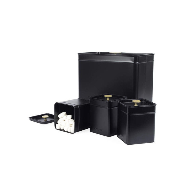 Set of three black metal kitchen storage tins with gold knobs, one open showing sugar cubes