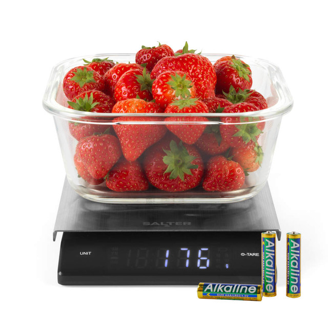 Glass bowl of strawberries on digital kitchen scale, LCD showing 176g, with AA batteries