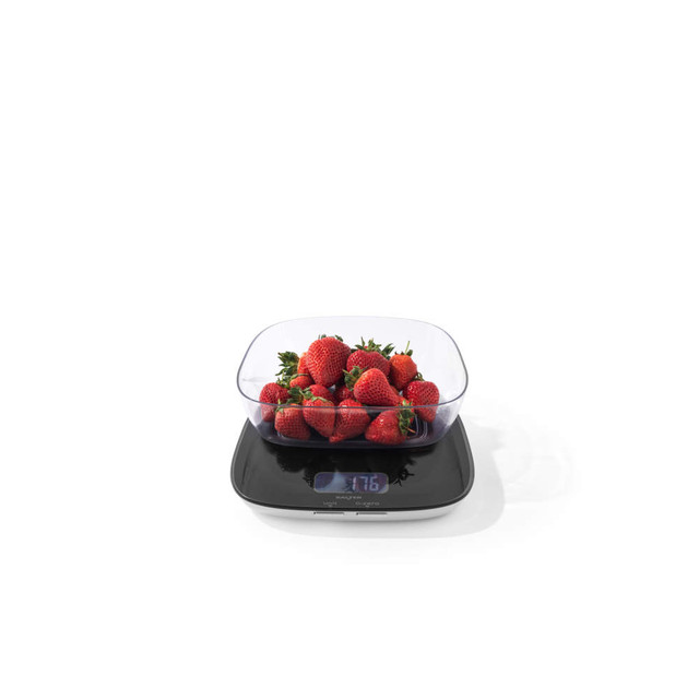 Kitchen scale with digital display weighing fresh strawberries in clear bowl
