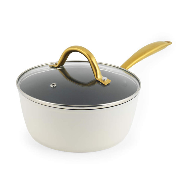 Cream saucepan with a glass lid and gold handle, angled side view