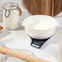 Digital kitchen scale with white mixing bowl, flour and baking tools on worktop