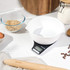 Digital kitchen scale with white mixing bowl, flour and baking tools on worktop
