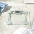 Glass digital bathroom scale with silver accents on tiled floor