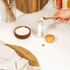 Clear pepper mill with wooden lid being refilled with black peppercorns on a kitchen counter