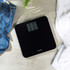 Black digital bathroom scale on tiled floor, near jeans and white towel