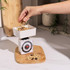 Hand pouring granola into a white mechanical kitchen scale on a wooden board.