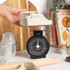 Black mechanical kitchen scale with clear bowl, shown on worktop with baking ingredients.