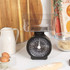 Black mechanical kitchen scale with clear bowl, shown on worktop with baking ingredients.