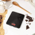 Black digital kitchen scale with red LED display on worktop, surrounded by chocolate pieces