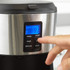 Hand pouring coffee beans into open black coffee machine, filter and scoop beside.