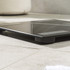 Black glass digital bathroom scale on tiled floor, showing low side profile.