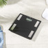 Black digital bathroom scale with silver sensors, top-down view on grey tiles.