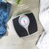 Mechanical bathroom scale with black platform on tiled floor, jeans and towel nearby
