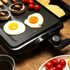 Electric grill with fried eggs, mushrooms, tomatoes and pancakes for breakfast