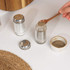 Glass salt and pepper shakers with metal lids, one being filled with ground pepper