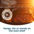 Oven thermometer in front of roast meat and potatoes on baking tray inside oven