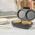 Black electric omelette maker open with two cooked omelettes inside, shown on kitchen counter