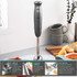 Silver stick blender blending tomato soup in saucepan, with fresh ingredients on table