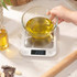 Digital kitchen scale with brushed metal platform on countertop next to baked cake