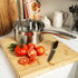 Stainless steel saucepan with lid on wooden chopping board beside fresh tomatoes and knife