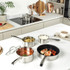 Stainless steel saucepan with lid on wooden chopping board beside fresh tomatoes and knife