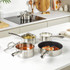 Set of stainless steel saucepans and frying pan on kitchen counter, food shown inside