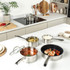 Set of stainless steel saucepans and frying pan on kitchen counter, food shown inside