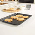 Grey non-stick baking tray with five chocolate chip cookies, shown in a modern kitchen.