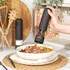Black electric pepper grinder dispensing onto steak salad, with matching salt mill beside