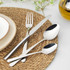 Hand holding silver fork with cake slice on plate, stoneware mug and cutlery nearby