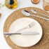 Neutral ceramic dinner plate on woven placemat with cutlery, coffee cup, and olive oil bottle