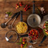 Non-stick saucepan set with lids and utensils on wooden table, filled with pasta and tomato sauce.