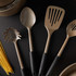 Set of gold kitchen utensils with black handles arranged on dark surface