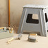 Grey plastic folding step stool with cleaning brushes and caddy, shown in a home setting