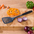 Black slotted spatula on wooden chopping board with sliced pepper and onion