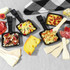 Raclette pans with mixed toppings, cheese and cured meats for tabletop serving.