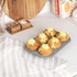 Grey muffin tray with five lemon-topped cupcakes, hand removing one, on kitchen counter