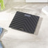 Black glass bathroom scale with striped pattern, shown on tiled floor