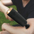 Black handheld massage gun in use on a person's arm outdoors