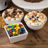 Three bowls of popcorn and sweets; popcorn topped with chocolate, caramel, and colourful candies.