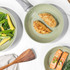 Set of two light green non-stick frying pans on hob, each with cooked food inside
