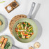 Non-stick frying pan with scrambled eggs and vegetables near buttered toast, kitchen setting