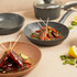 Grey non-stick saucepan and frying pan set shown with cooked skewers, kitchen setting